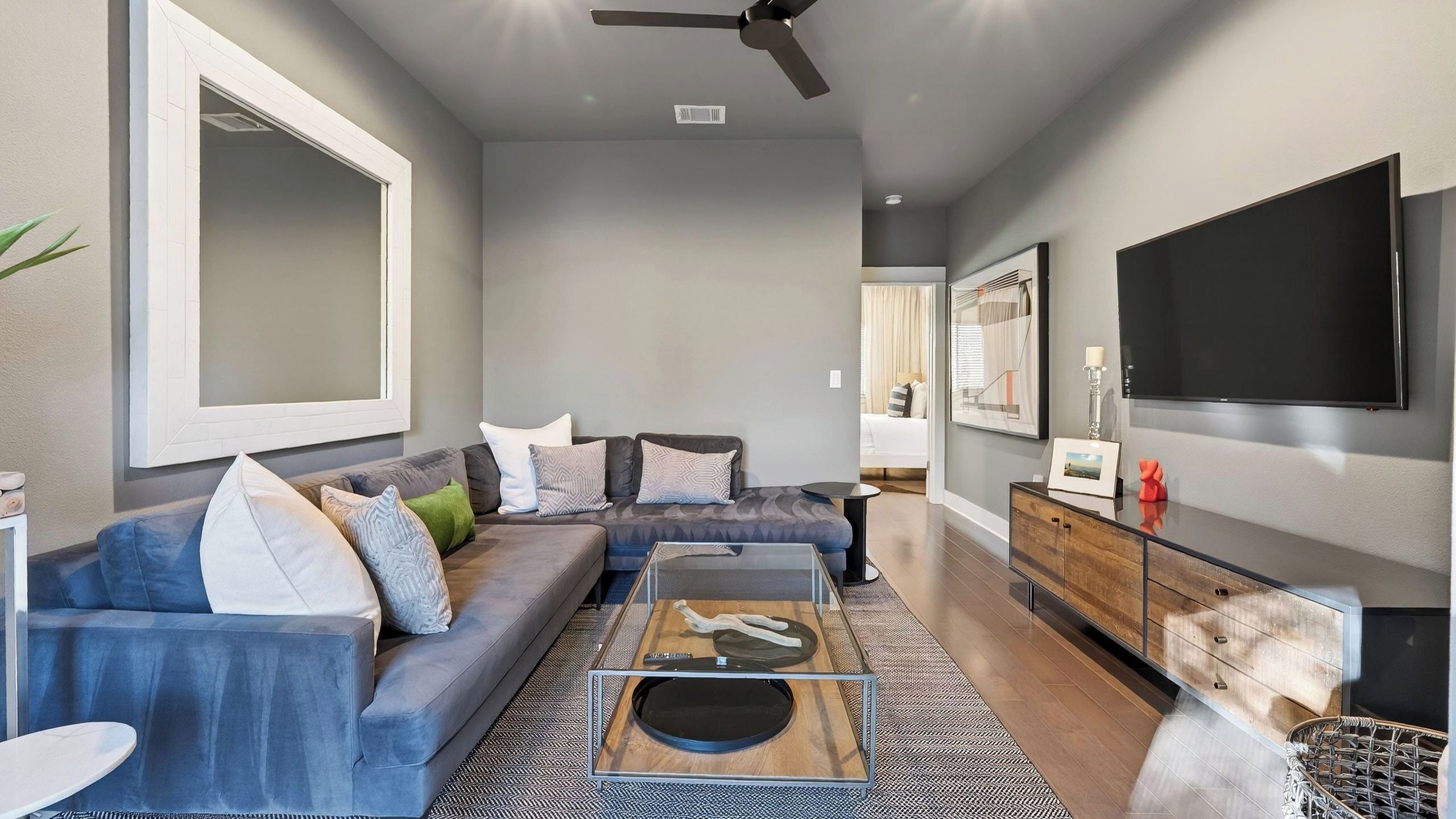 A modern living room with a sofa, coffee table, TV, and a ceiling fan.