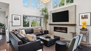 Ein modernes Wohnzimmer mit einem schwarzen Ledersofa, einem Glastisch, einem Kamin und großen Fenstern.