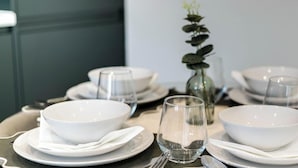 A dining table set with white bowls, plates, and cutlery, and a clear glass. - Stylish 1-Bed Apartment in Croydon | Easy Access to Central London (South Croydon)