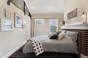Ein Schlafzimmer mit Bett, Fenster, Kamin und Wandbildern.