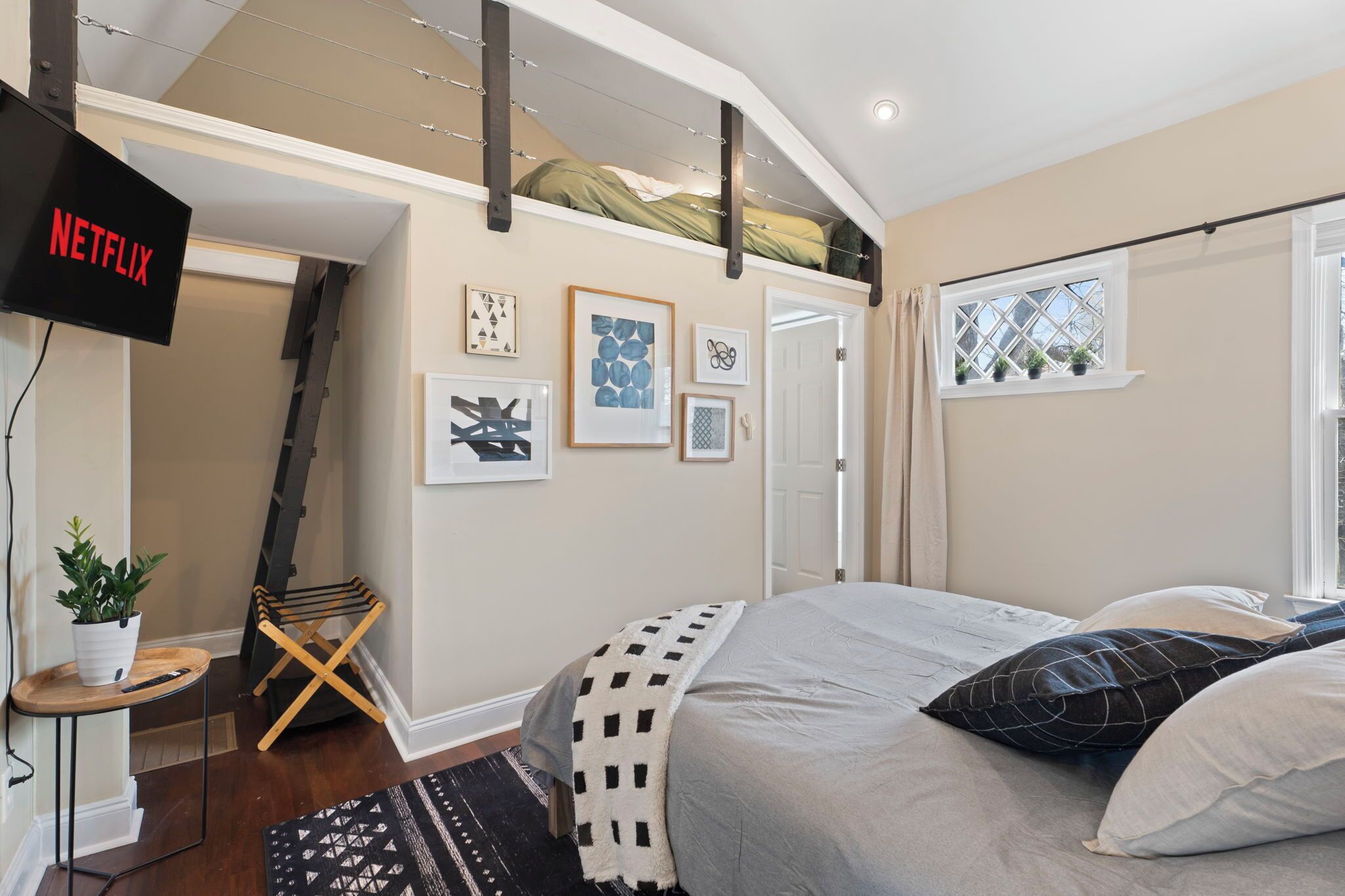 Une chambre à coucher avec un lit, un téléviseur fixé au mur et une fenêtre avec des rideaux.