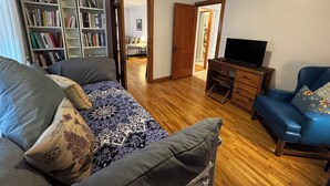 Una sala de estar con sofá, mesa de centro, estantería, escritorio con computadora y televisor.