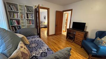 A living room with a sofa, a coffee table, a bookshelf, a desk with a computer, and a television.
