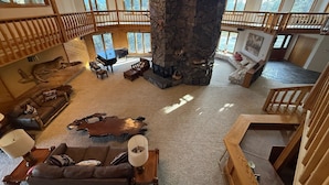 A spacious living area with a stone fireplace, a piano, and a high ceiling with a fan. - Eagle's Bluff Estate on Flathead Lake near Glacier National Park (Polson)