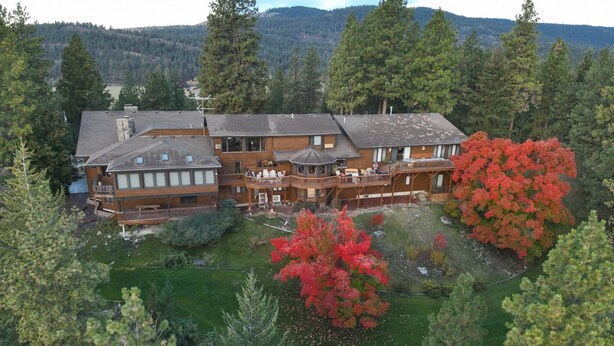 A large, multi-story wooden building with a deck and outdoor seating area, surrounded by dense forest and a lake. - Eagle's Bluff Estate on Flathead Lake near Glacier National Park (Polson)