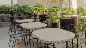 Eine Terrassengaststätte mit runden Tischen und Stühlen, umgeben von Blumentöpfen und einem Baum.