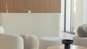 Ein modernes Wohnzimmer mit Sofa, Hocker und Couchtisch, einer Wand mit Holzlatten und einem großen Fenster.