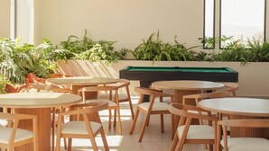 Ein stilvoller Lounge-Bereich mit mehreren runden Tischen und Sesseln, einem Billardtisch und Kübelpflanzen.
