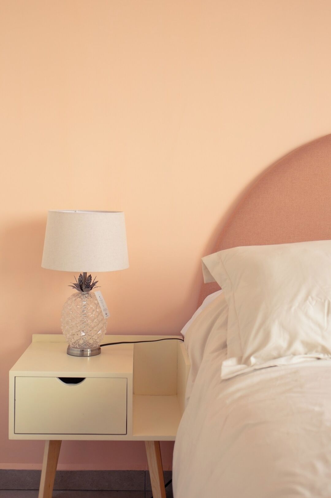 A bed with white linens, a nightstand with a lamp, and a wooden floor.