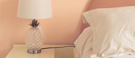 A bed with white linens, a nightstand with a lamp, and a wooden floor.