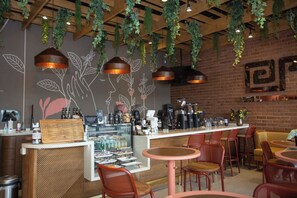 L’intérieur d’un café, avec des plantes suspendues, un comptoir où l’on sert du café et des espaces aménagés pour s’asseoir.