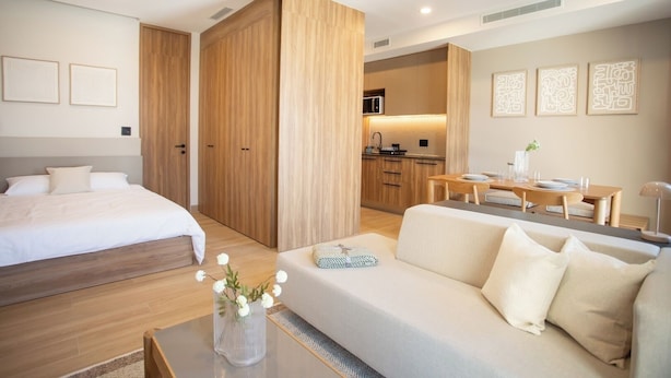 Ein modernes Hotelzimmer mit Bett, einer Couch, einem Esstisch und einer Küchenzeile.