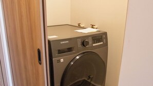 Eine kompakte, moderne Waschmaschine in einem kleinen Waschraum mit Holzboden und weißer Wand.