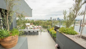 Terraço moderno ao ar livre com área de refeições, plantas em vasos e vista para a paisagem urbana.
