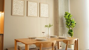 En matplats med ett träbord dukat för fyra personer, tre inramade abstrakta konstverk, en hög vas med blommor och en grön växt.