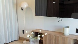 Ett modernt vardagsrum med en platt-TV, ett soffbord i trä med en vas med blommor, en golvlampa och en soffa.