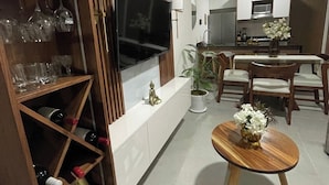 Un soggiorno moderno con televisione, scaffali in legno, zona pranzo e cucina sullo sfondo.