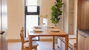 A dining area with a wooden table set for four, a potted plant, and a view of a door and window. - Mr W | 1BR Margot Loft Modern City Tower (Guadalajara)