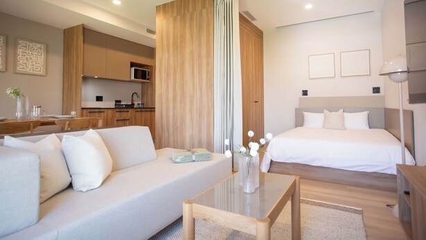A modern hotel room with a sofa, a bed, a small table, and a kitchen area in the background. - Mr W | 1BR Margot Loft Modern City Tower (Guadalajara)