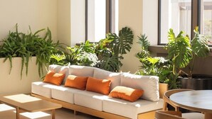 Un intérieur moderne avec un canapé, des fauteuils et des tables, le tout baigné de lumière grâce à de grandes fenêtres et agrémenté de plantes d’intérieur.