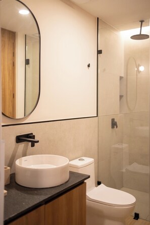 Une salle de bain moderne avec un lavabo rond, des toilettes et une douche séparée par une paroi en verre.