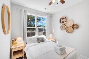 Une chambre d’hôtel comprenant un lit, une table de chevet avec une lampe, une fenêtre avec des rideaux et des éléments de décoration murale.