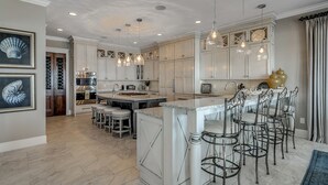 A spacious kitchen with white cabinetry, a large island with bar stools, pendant lighting, and a view of the dining area.