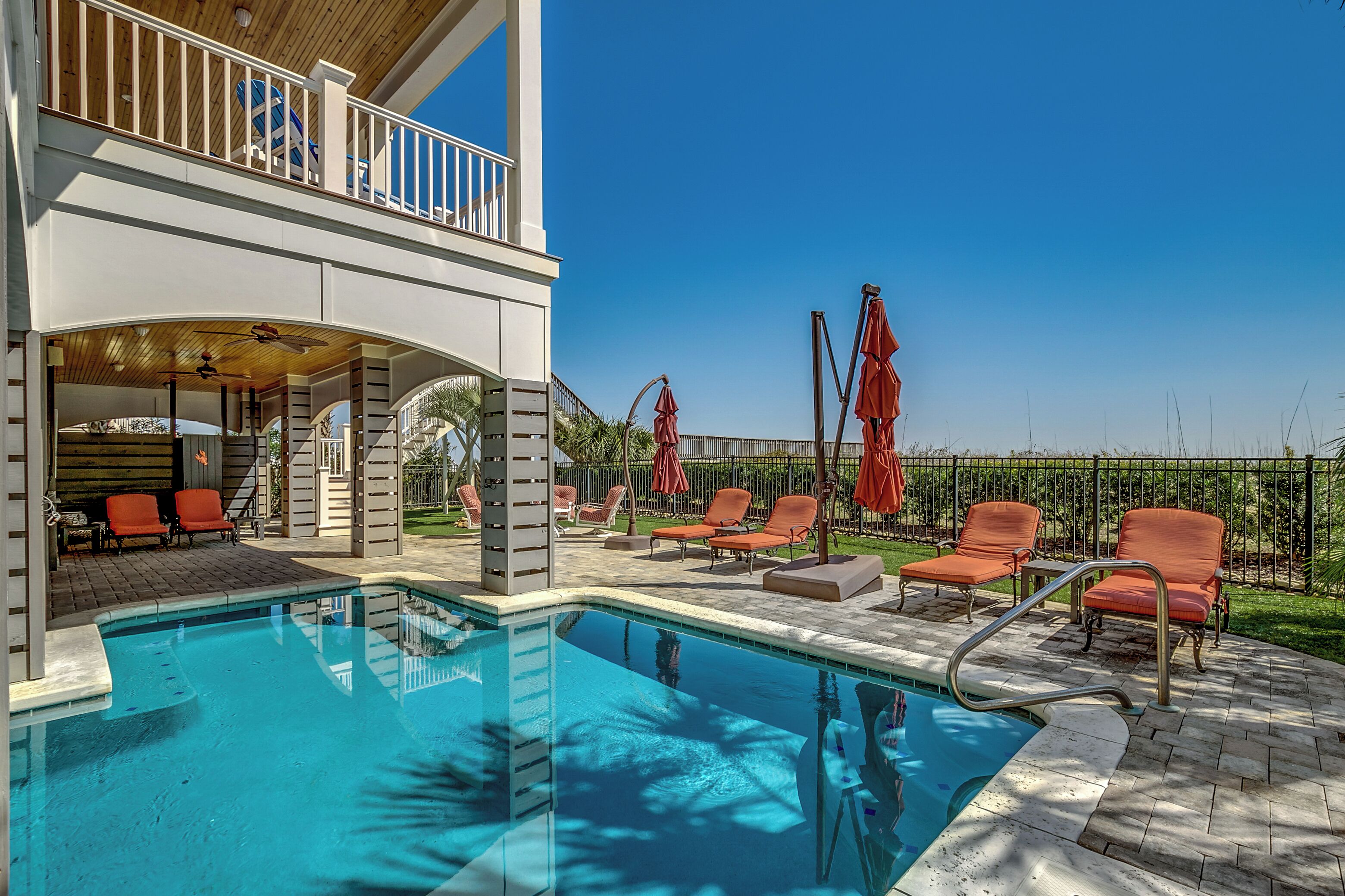 Ein Schwimmbecken mit Liegestühlen und Sonnenschirmen, eine überdachte Terrasse und ein eingezäunter Außenbereich.