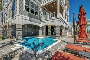 A pool area with a clear blue pool, lounge chairs, and a covered seating area.