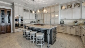A kitchen with white cabinetry, a central island with stools, stainless steel appliances, and pendant lighting.