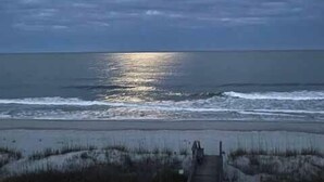 A wooden boardwalk leading to a beach with a calm sea and a clear sky.