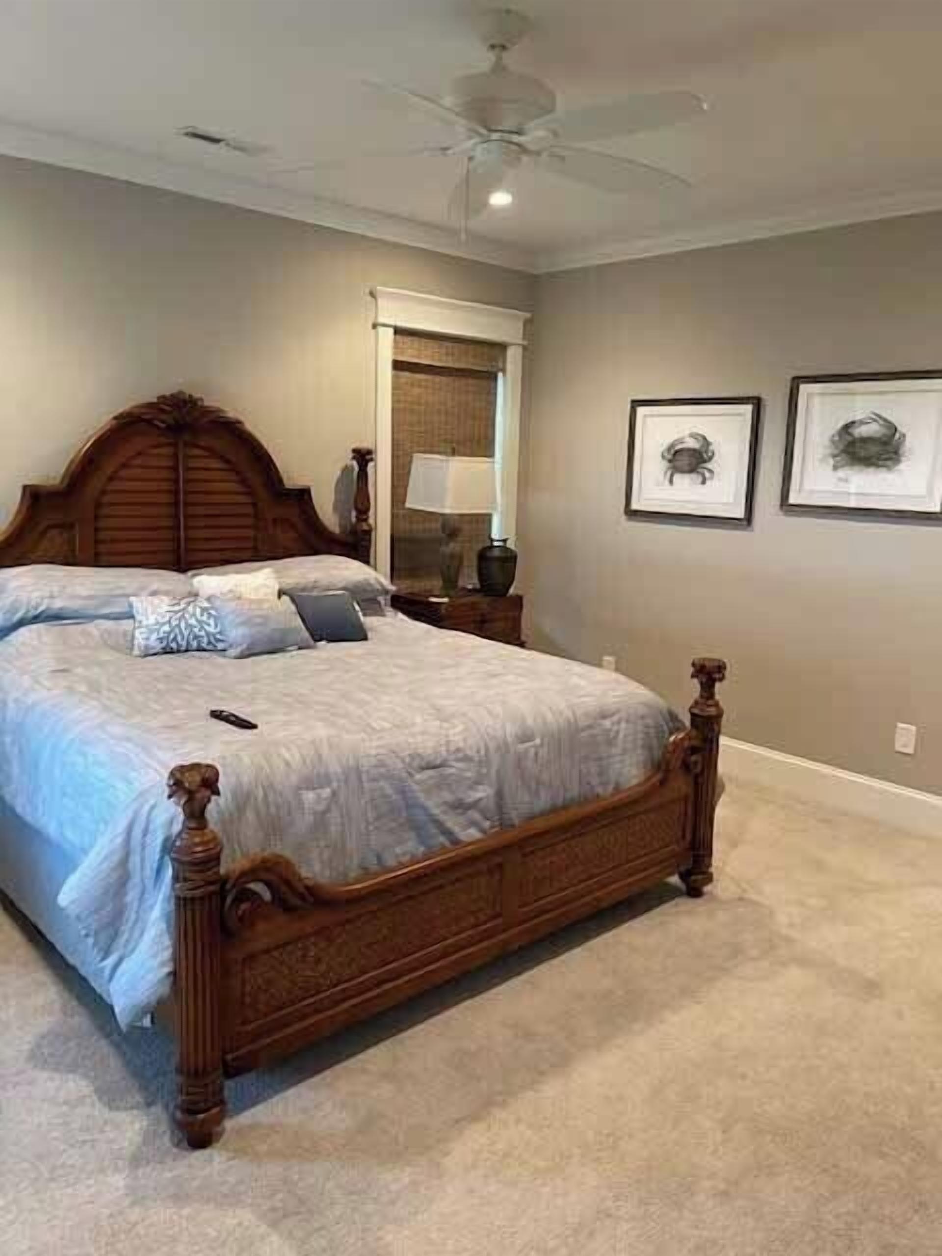 A bedroom with a large bed, a ceiling fan, a nightstand, and two framed pictures on the wall.