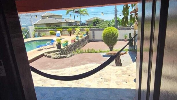 Uma entrada que dá para um pátio com piscina, rede e vista para uma área residencial.