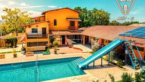 Um edifício de dois andares com piscina, escorregador e área de varanda coberta.