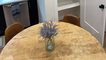 A dining area with a round table, a vase with flowers, a kitchen with cabinets, and a white door.