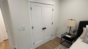 A bedroom with a bed, a nightstand, a lamp, a wall-mounted shelf, and a wardrobe. - 2-bedroom apartment in Utah County (American Fork)
