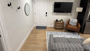 A modern bedroom with a bed, a TV, a small wooden side table, and a door leading to another room. - 2-bedroom apartment in Utah County (American Fork)
