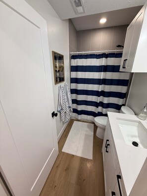 A small bathroom with a white door, a striped shower curtain, a white sink, and a wooden floor. - 2-bedroom apartment in Utah County (American Fork)