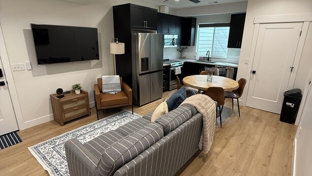 A modern living room with a sofa, a dining table, a kitchen area, and a TV mounted on the wall. - 2-bedroom apartment in Utah County (American Fork)