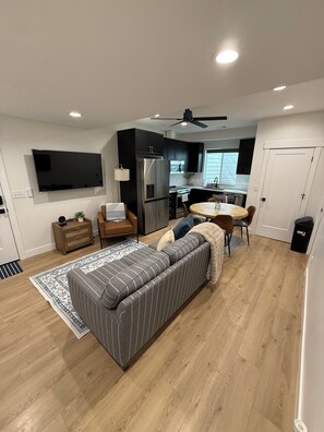A modern living room with a sofa, a dining table, a kitchen area, and a TV mounted on the wall. - 2-bedroom apartment in Utah County (American Fork)