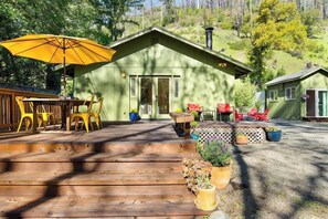Une terrasse en bois avec des meubles d’extérieur, un patio couvert et un petit bâtiment à l’extérieur peint en vert.