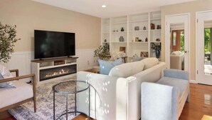 A living room with a flat-screen TV, a fireplace, a sofa, and a bookshelf. - Wine Country Creekside Cottage Bridge & Day Studio (Kenwood)