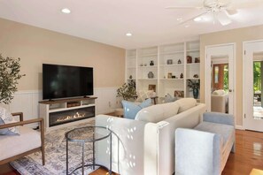 A living room with a flat-screen TV, a fireplace, a sofa, and a bookshelf. - Wine Country Creekside Cottage Bridge & Day Studio (Kenwood)