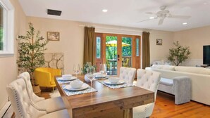A dining area with a wooden table set for four, surrounded by white upholstered chairs. - Wine Country Creekside Cottage Bridge & Day Studio (Kenwood)