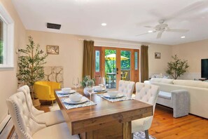 A dining area with a wooden table set for four, surrounded by white upholstered chairs. - Wine Country Creekside Cottage Bridge & Day Studio (Kenwood)