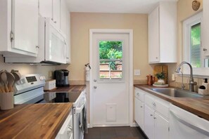 A compact kitchen with white cabinets, a wooden countertop, a built-in oven, and a window with a view of greenery. - Wine Country Creekside Cottage Bridge & Day Studio (Kenwood)