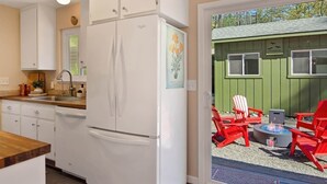 A kitchen with white cabinets, a refrigerator, and a dining area with red chairs and a fire pit. - Wine Country Creekside Cottage Bridge & Day Studio (Kenwood)