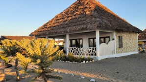 Ein Gebäude mit einem Reetdach, weißer Fassade, einer kleinen Veranda und einem Garten mit gelb blühenden Pflanzen.