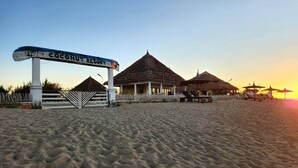 A beach resort with a sign reading 'Coconut Resort,' a thatched-roof building, and a sandy beach.