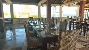 A long dining table with chairs, set for a meal, in a covered outdoor area with a view of the sea. - Private Villa with Sea View & Whirlpool Tub (201) (Soalara Bas)